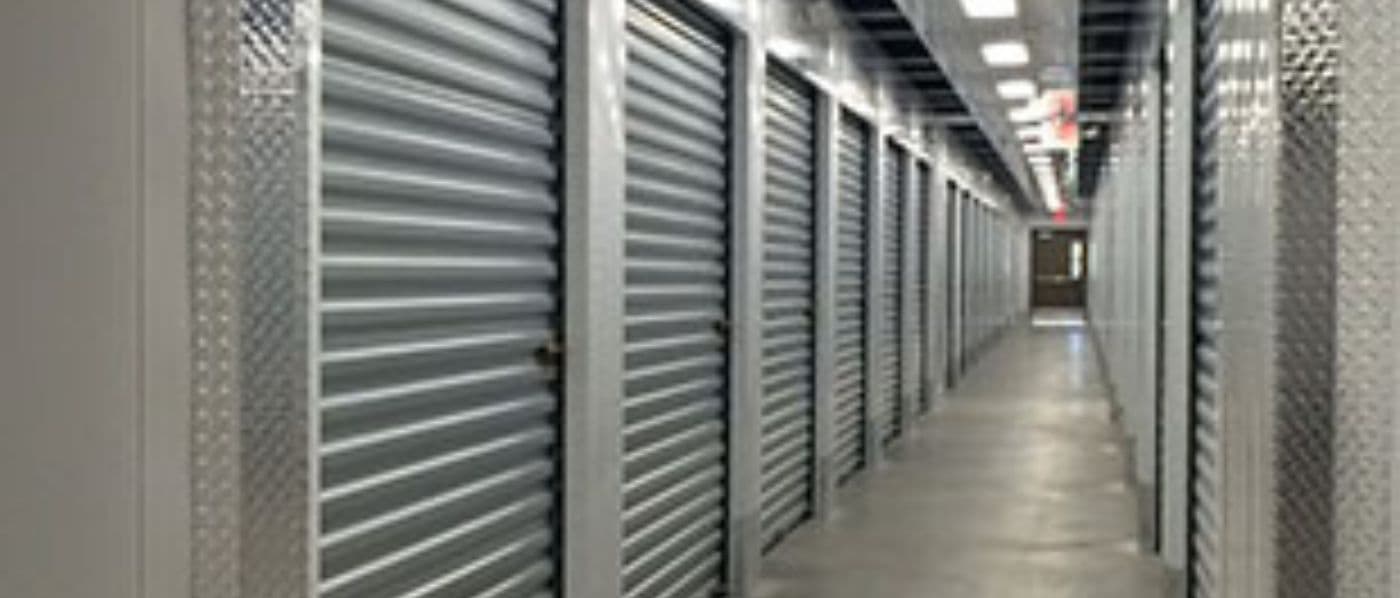 Brightly lit indoor hallway lined with roll-up storage unit doors